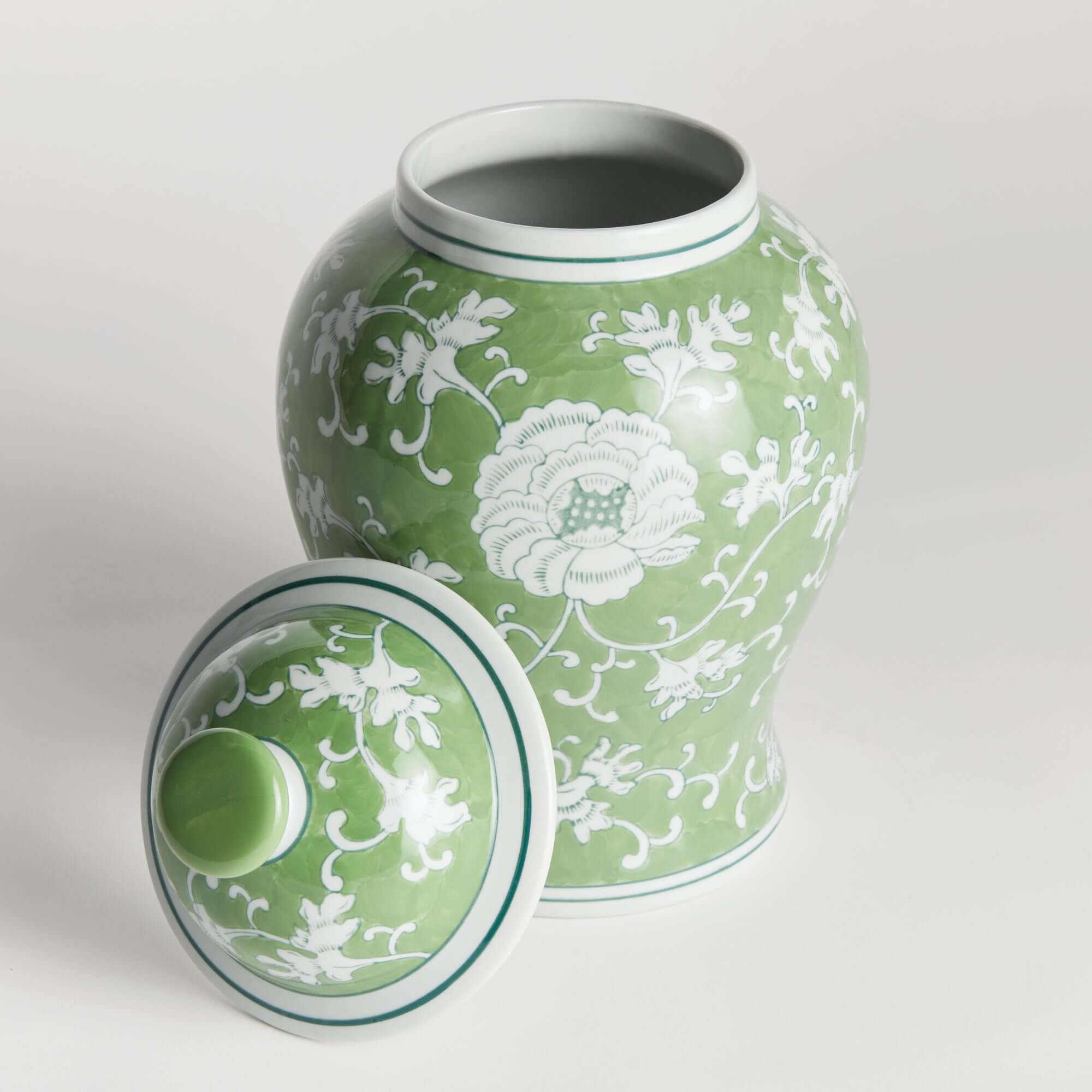 Green ceramic jar with white floral patterns on a light gray background