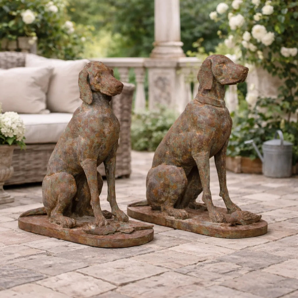 Two rusted metal dog statues on a patio with outdoor furniture and plants in the background.