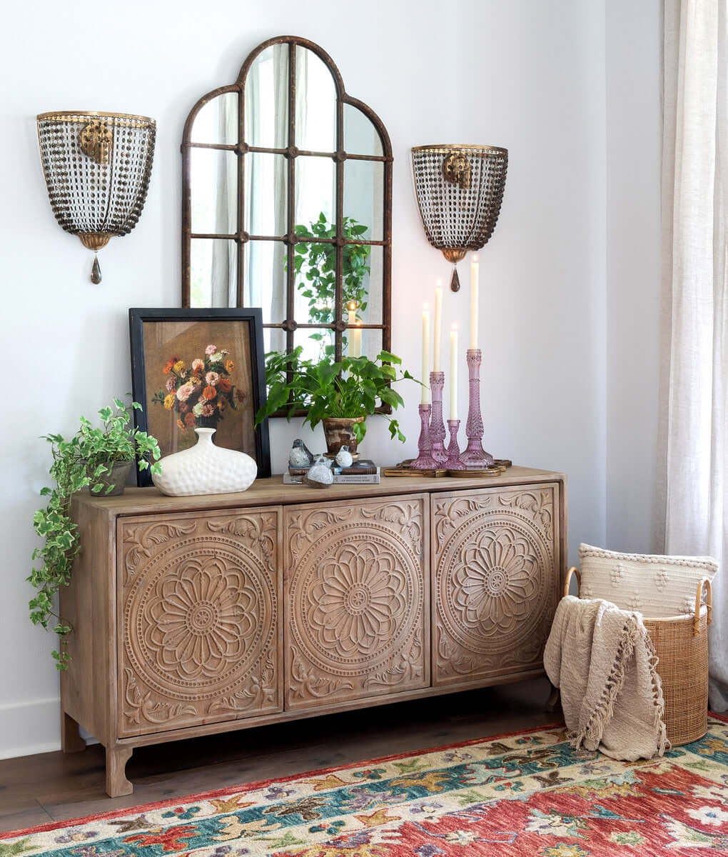 Decorative sideboard with ornate design, mirror, and wall sconces in a room setting.