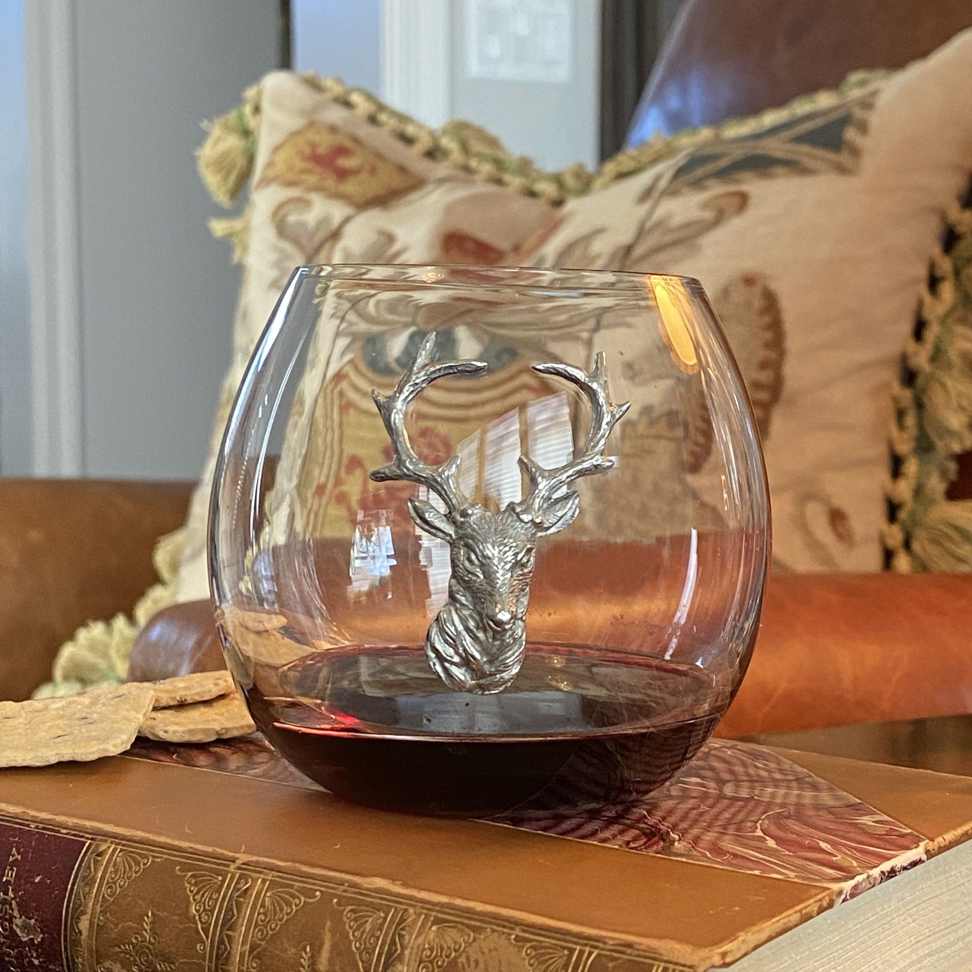 Glass tumbler with deer head design on a wooden surface with decorative pillows in the background