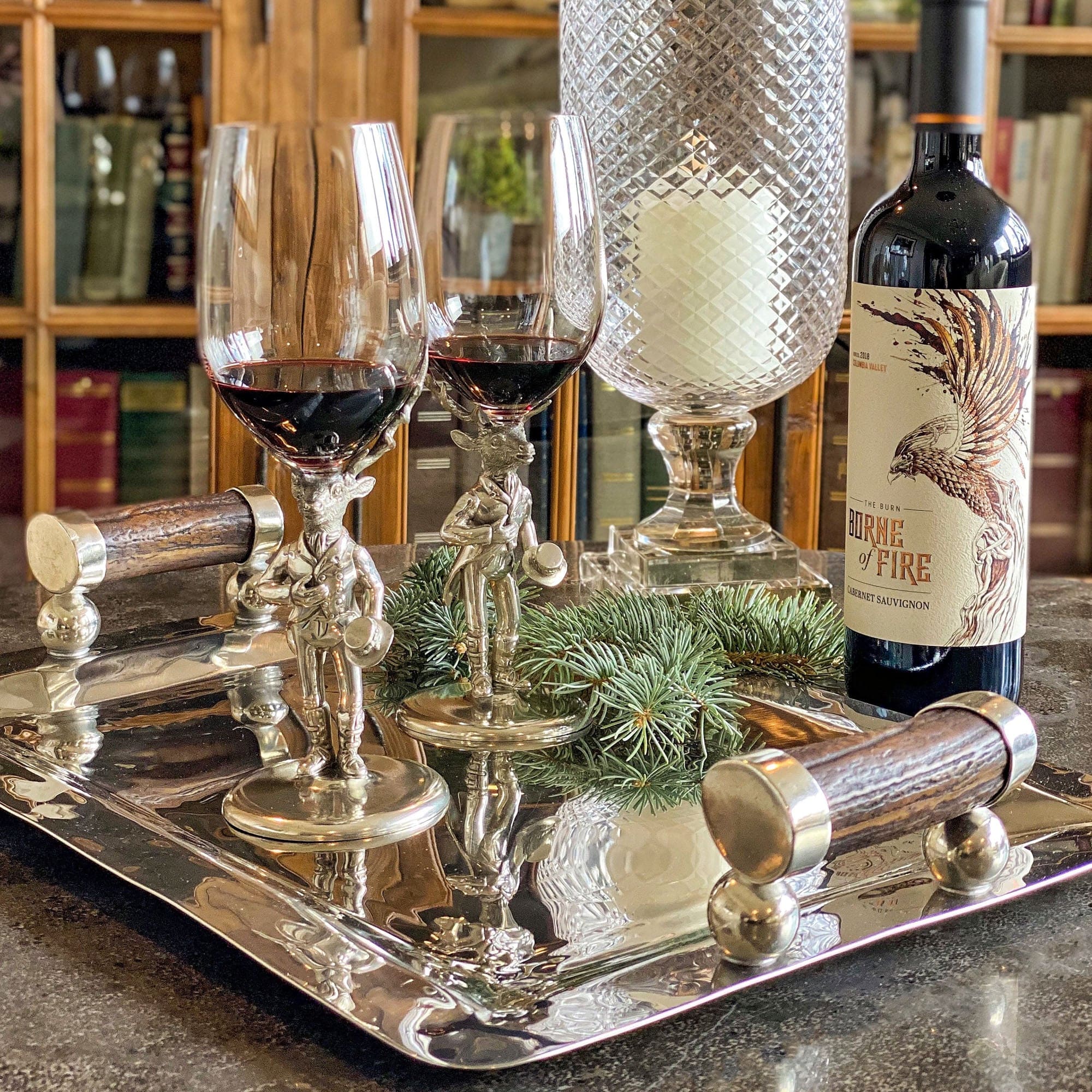Gentleman Elk Wine glasses with red wine on a silver tray, accompanied by a bottle of wine and decorative elements.