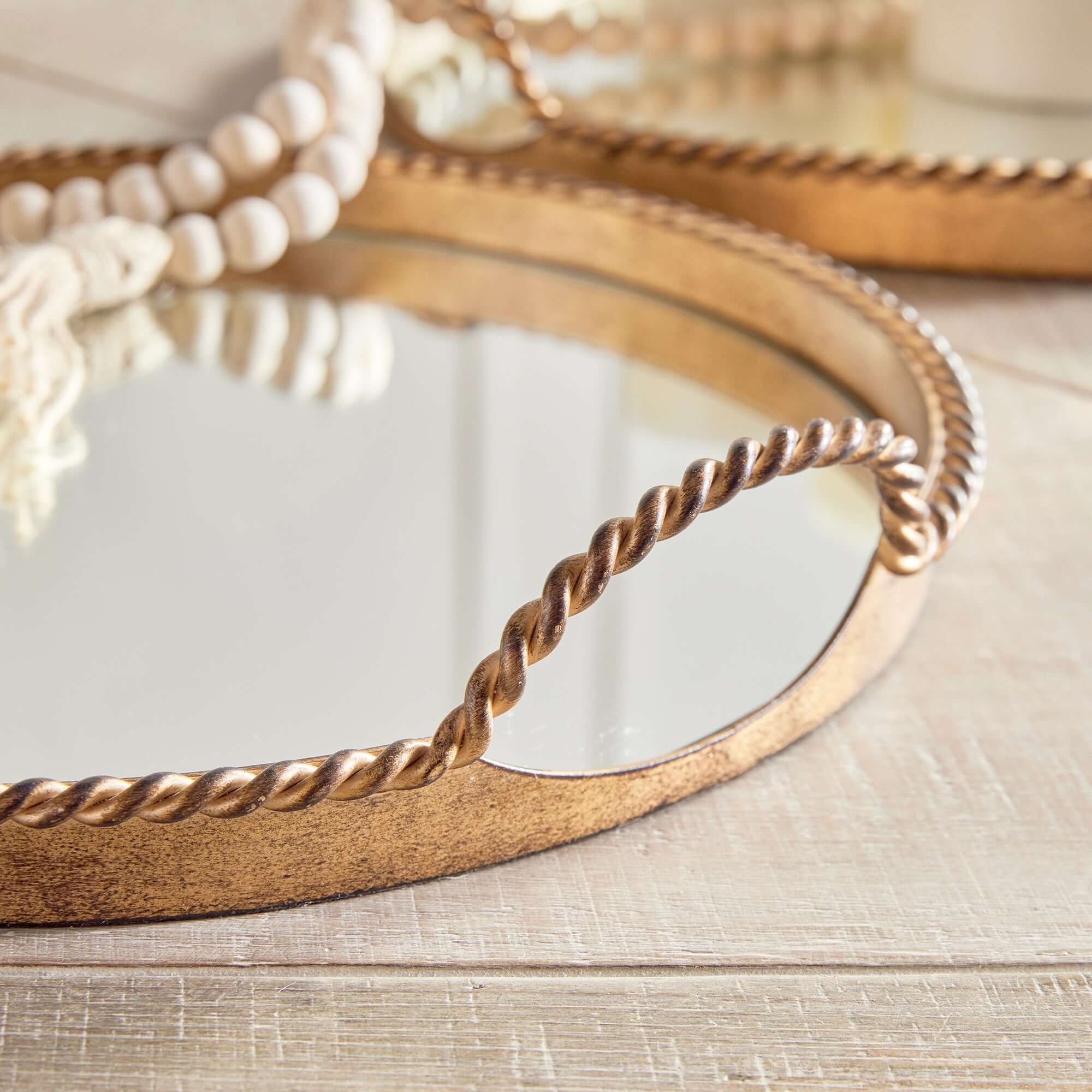 Round gold mirror with twisted design on a wooden surface
