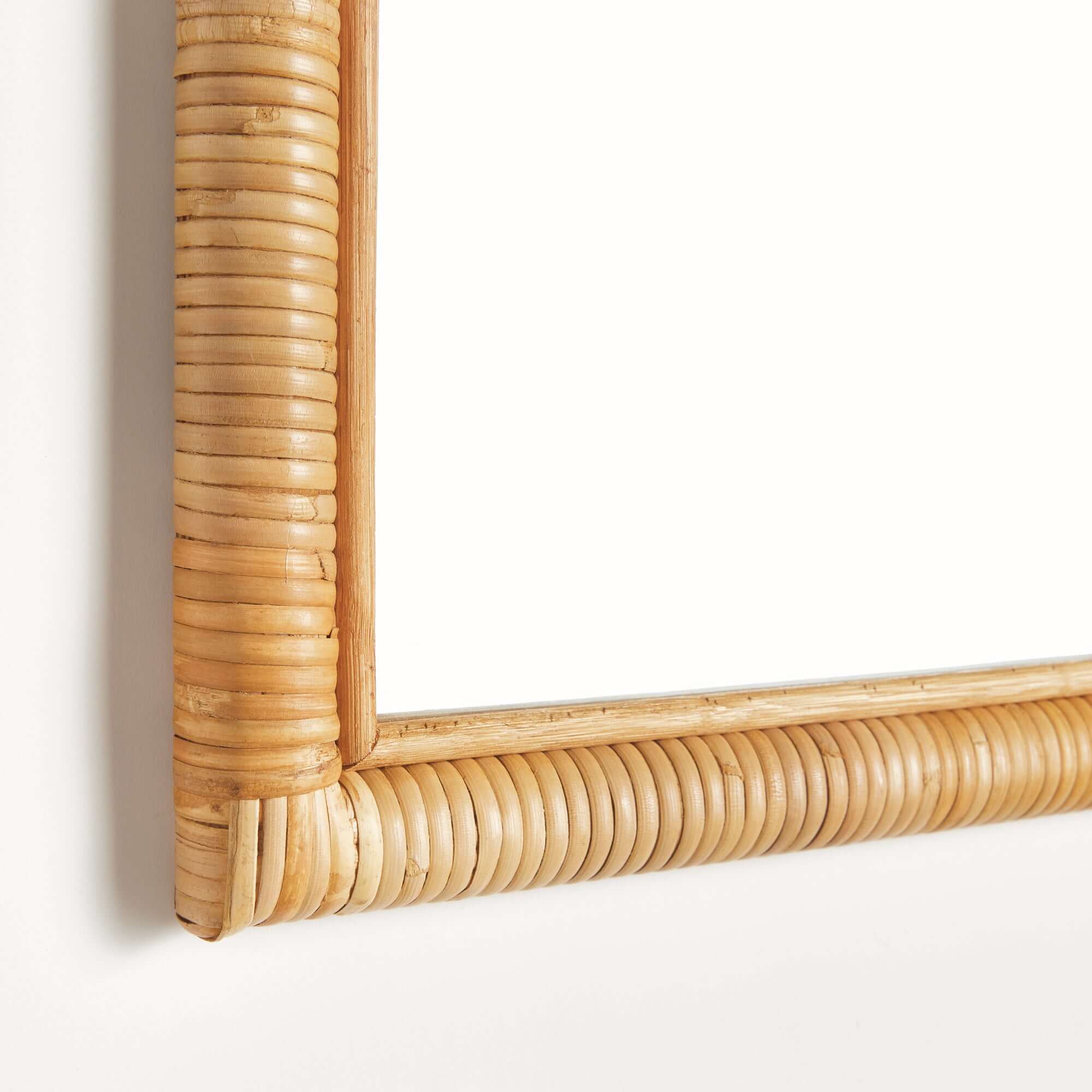 Close up of the corner of an arched mirror with a wicker frame on a white background