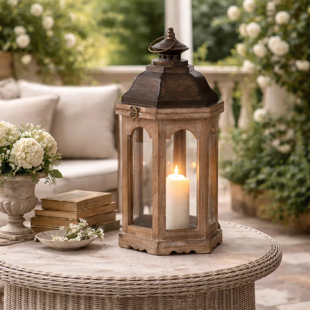 Wooden lantern with a lit candle on a table outdoors, surrounded by flowers and books.