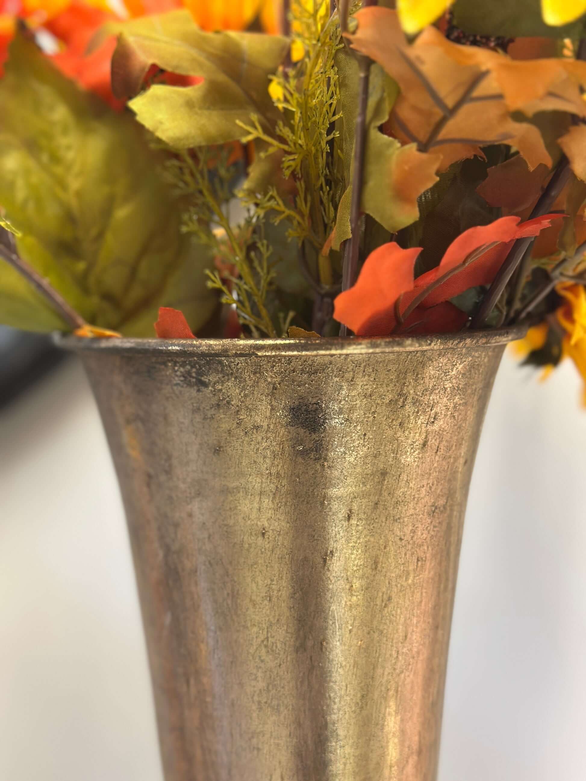 Metallic vase with autumn-themed artificial leaves on a white background