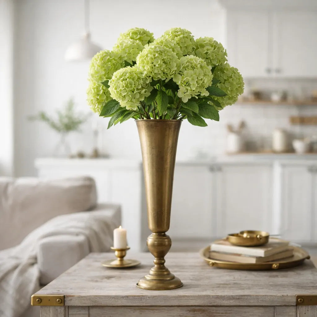 Decorative gold trumpet vase with green flowers on a wooden table in a living room setting.