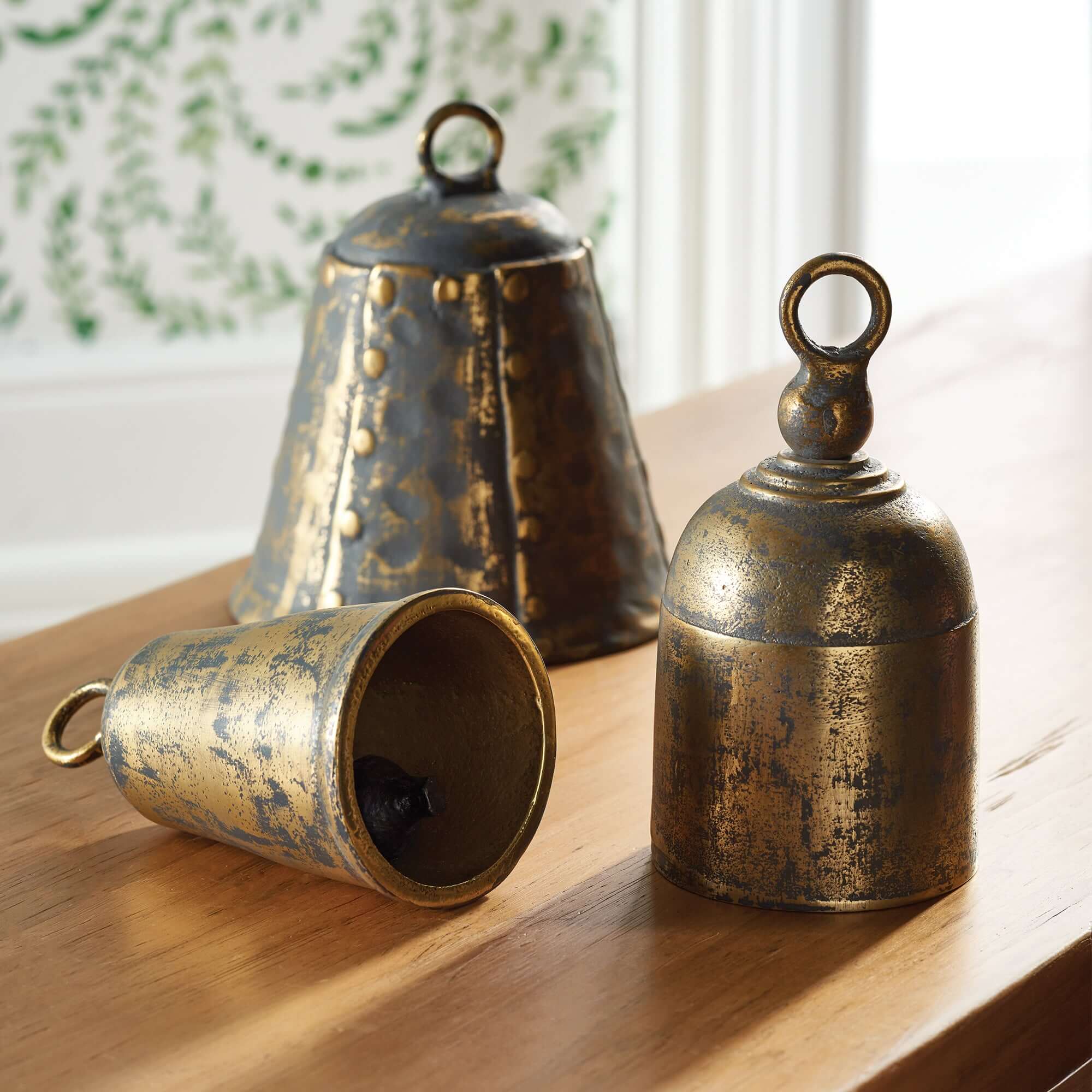 Three rustic brass bells on a wooden surface with a blurred decorative background