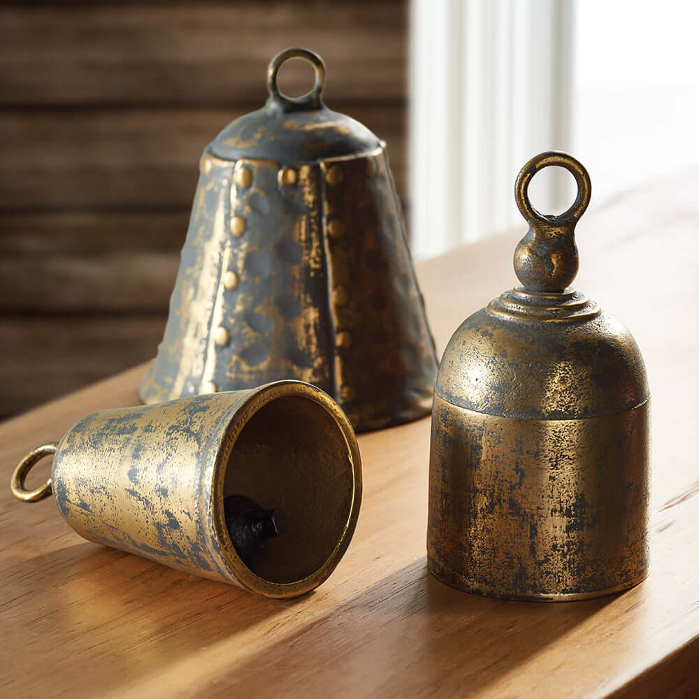 Three rustic metal bells on a wooden surface with a blurred background