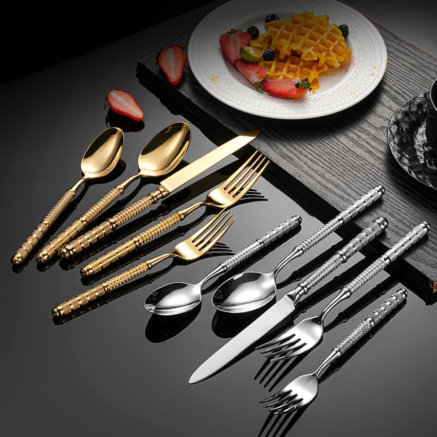 Gold and silver cutlery set on a dark surface with a plate of waffles and strawberries.
