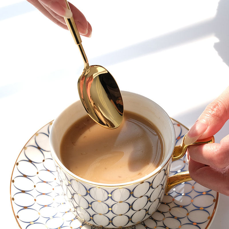 Gold spoon stirring coffee in a patterned cup on a matching saucer.