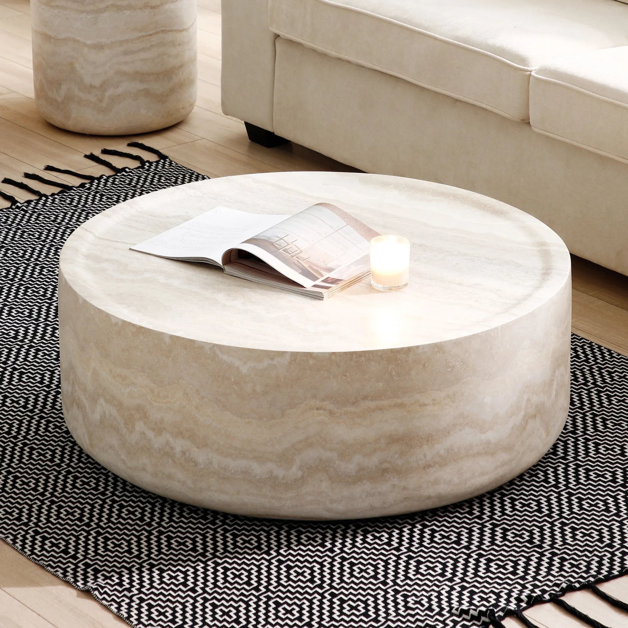 Marble-Effect Round Fiberglass Coffee Table with a candle and magazine on a patterned rug in a living room.