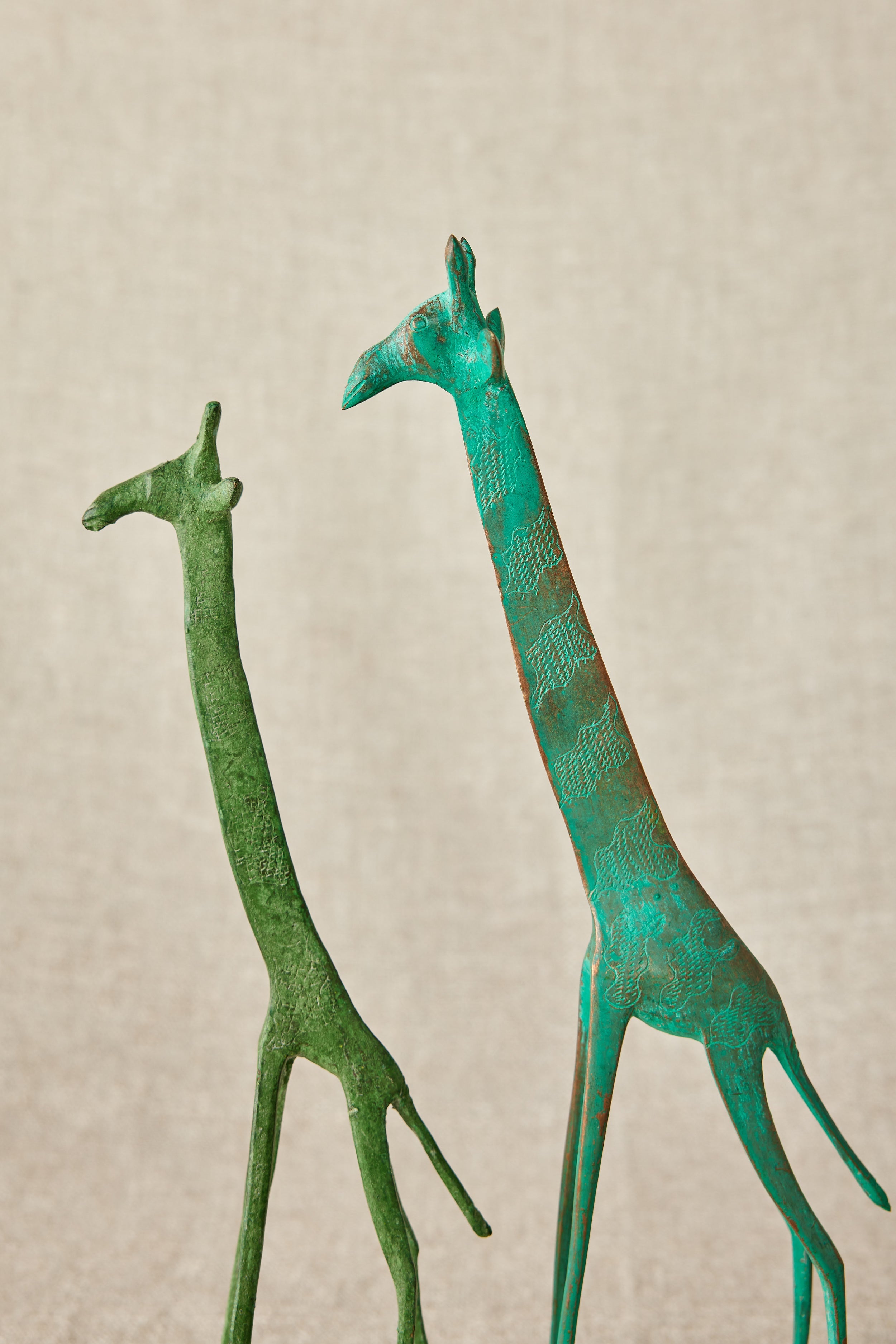Two green metal giraffe sculptures on a beige background