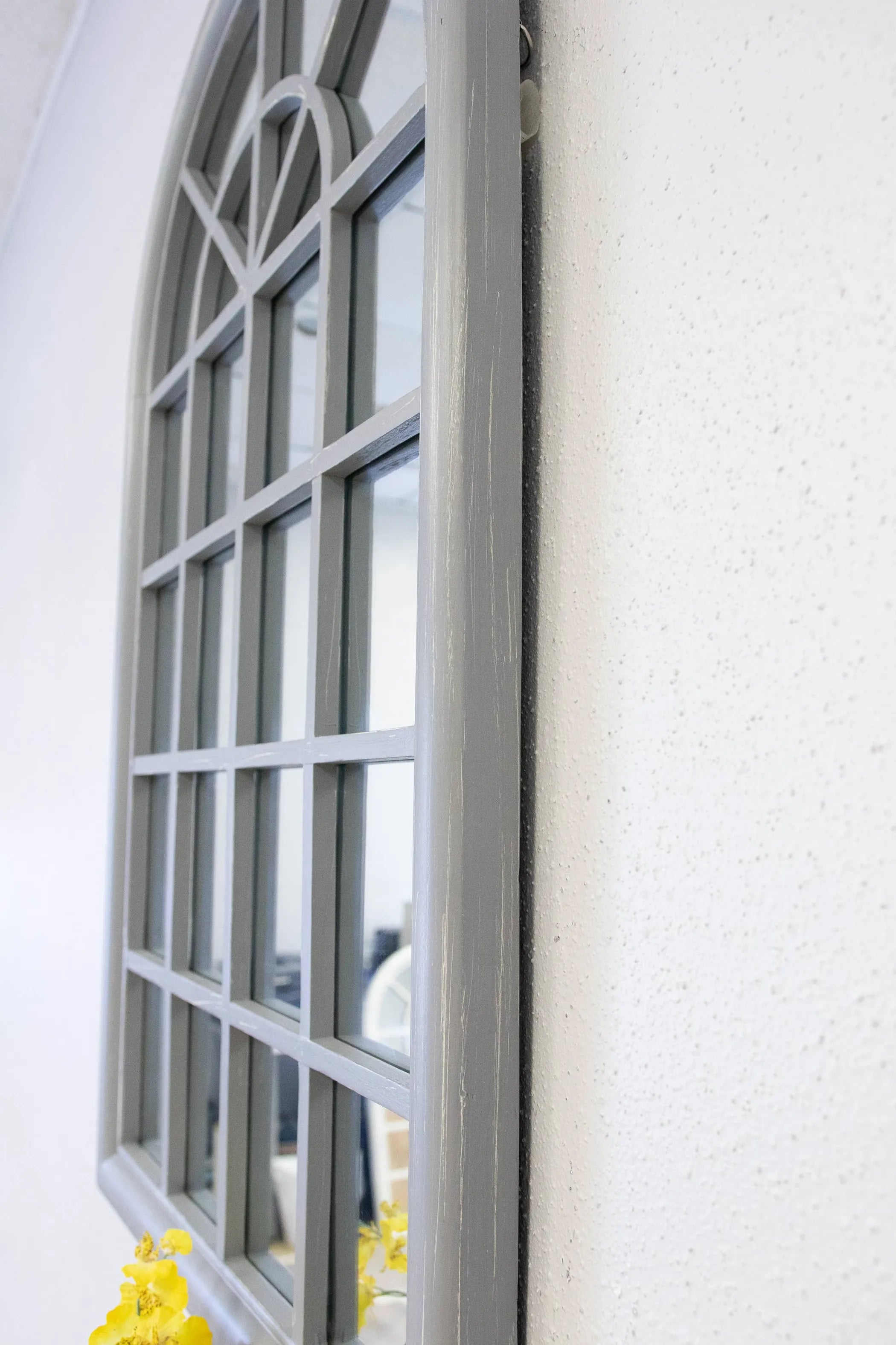 Side angle of arched window pane mirror on a white wall