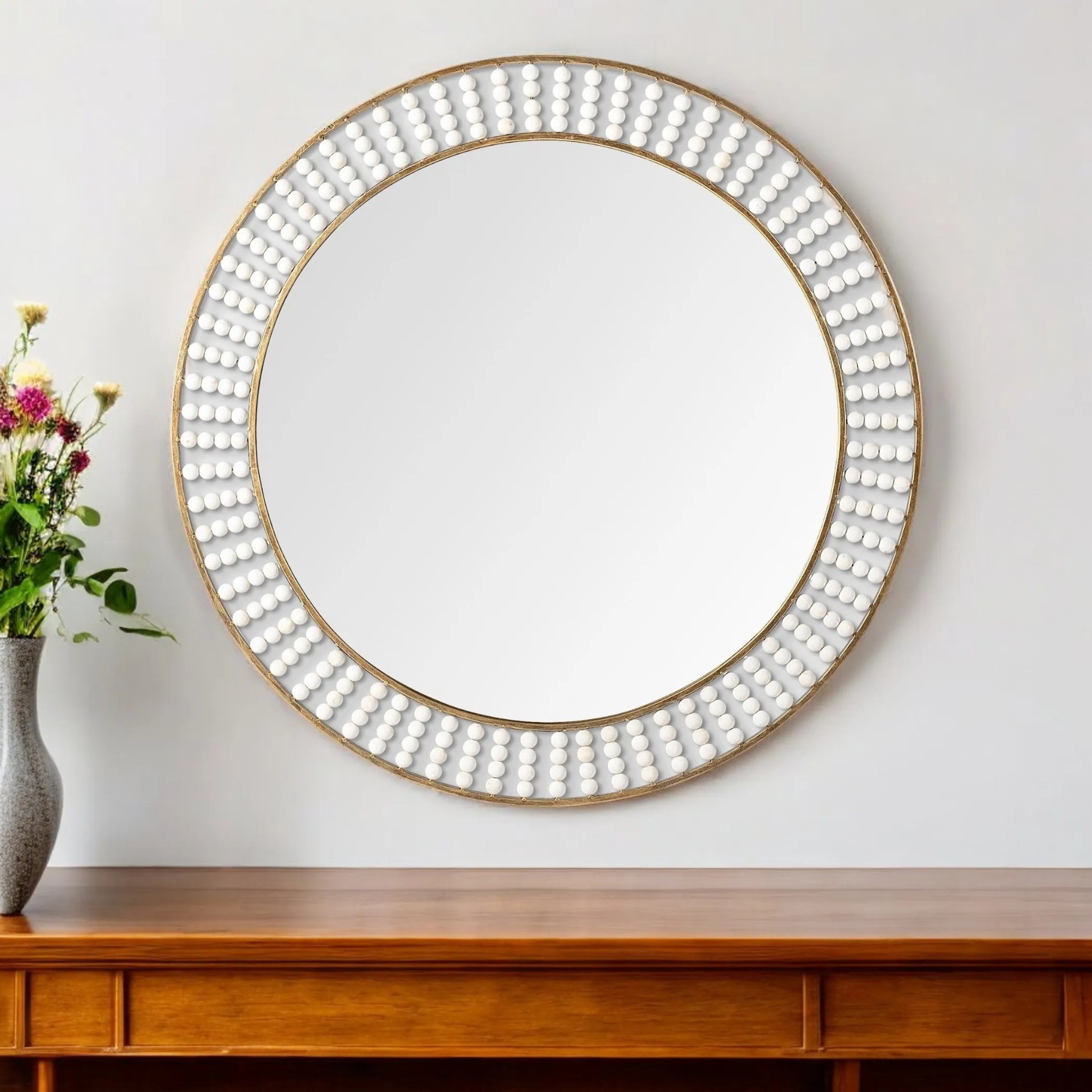 Round decorative mirror with a gold frame on a white wall above a wooden console table.