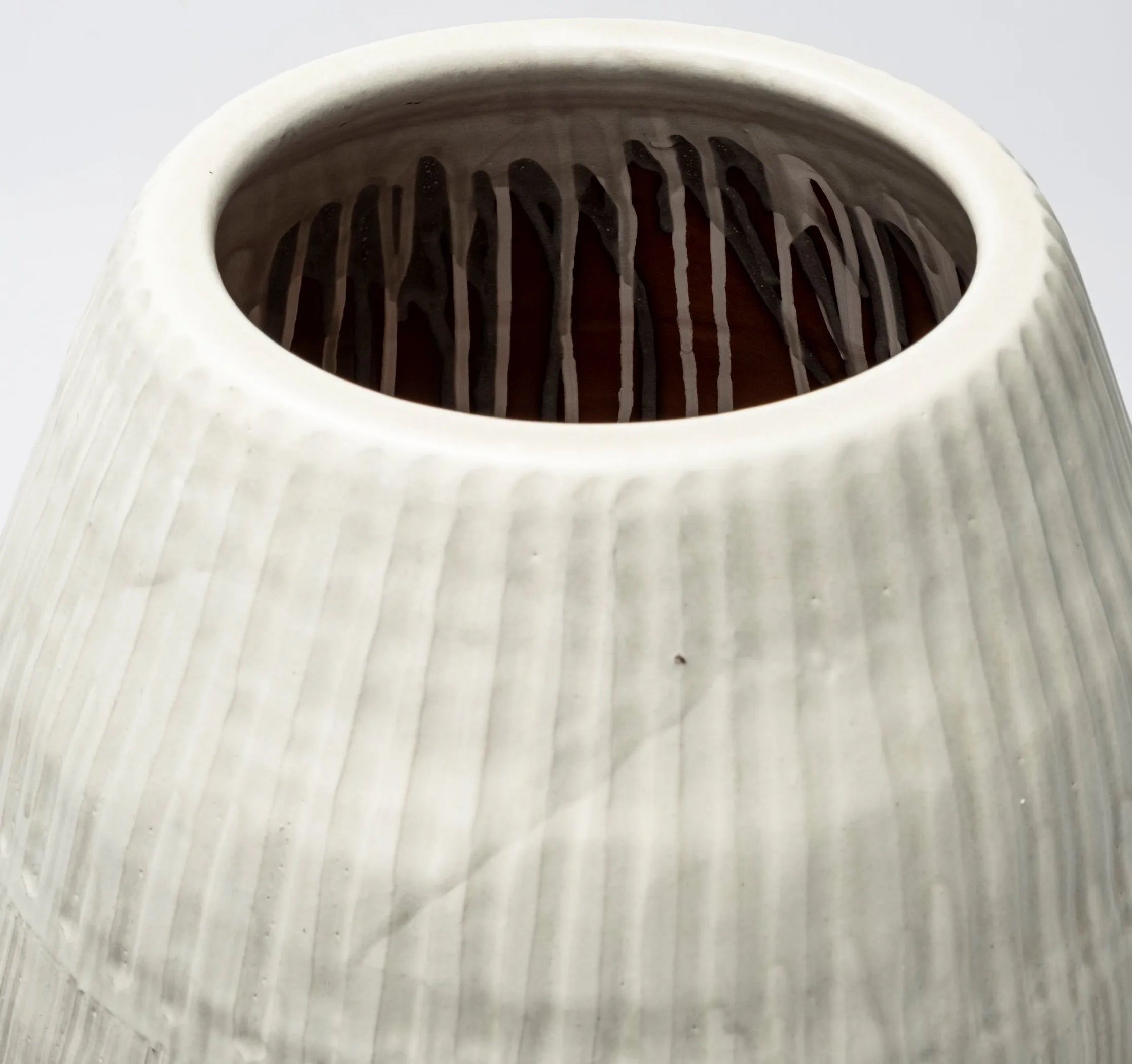 Close-up of a textured ceramic vase with a white exterior and dark interior.