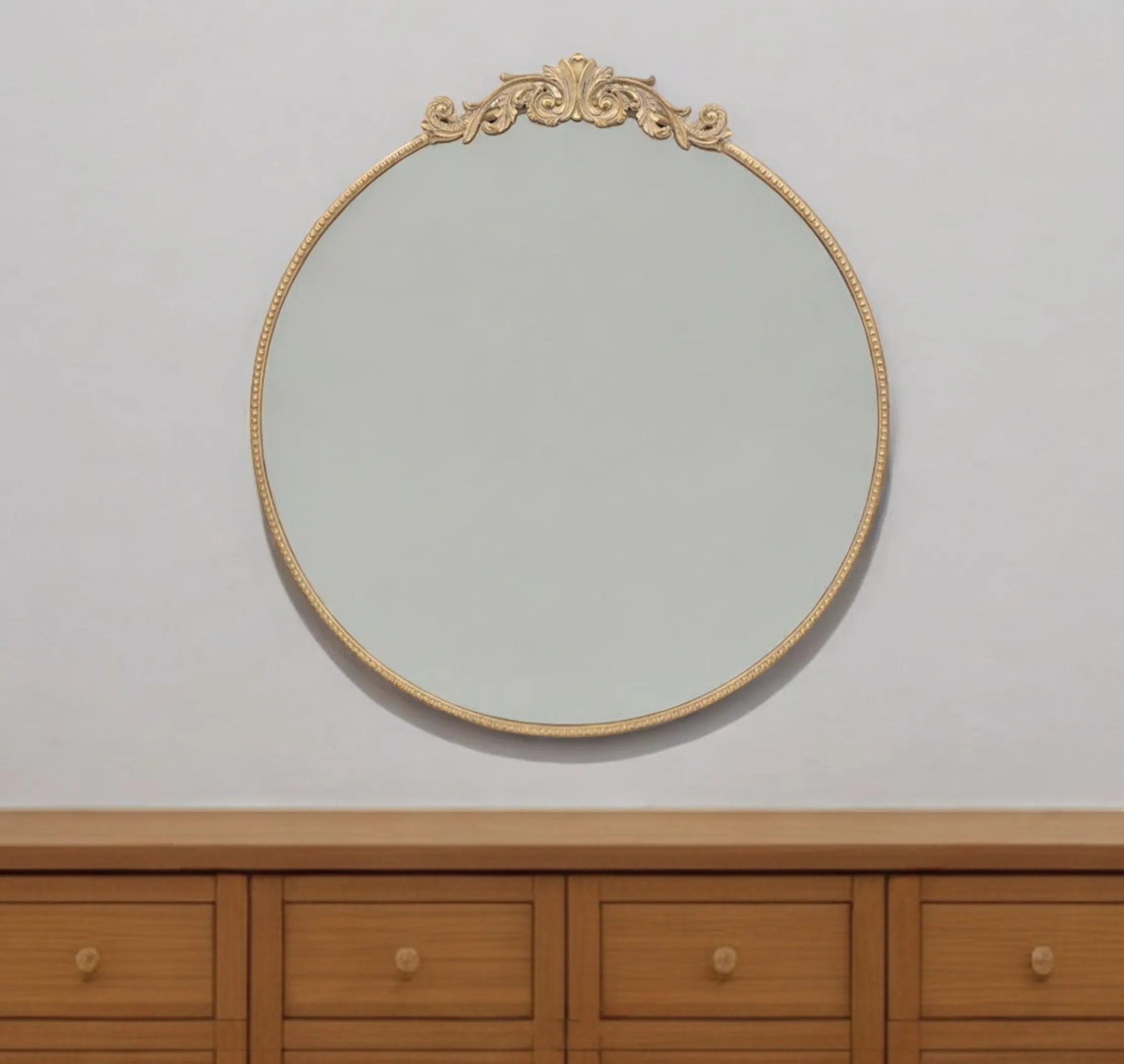 Decorative round mirror with gold frame on a white wall above wooden furniture.