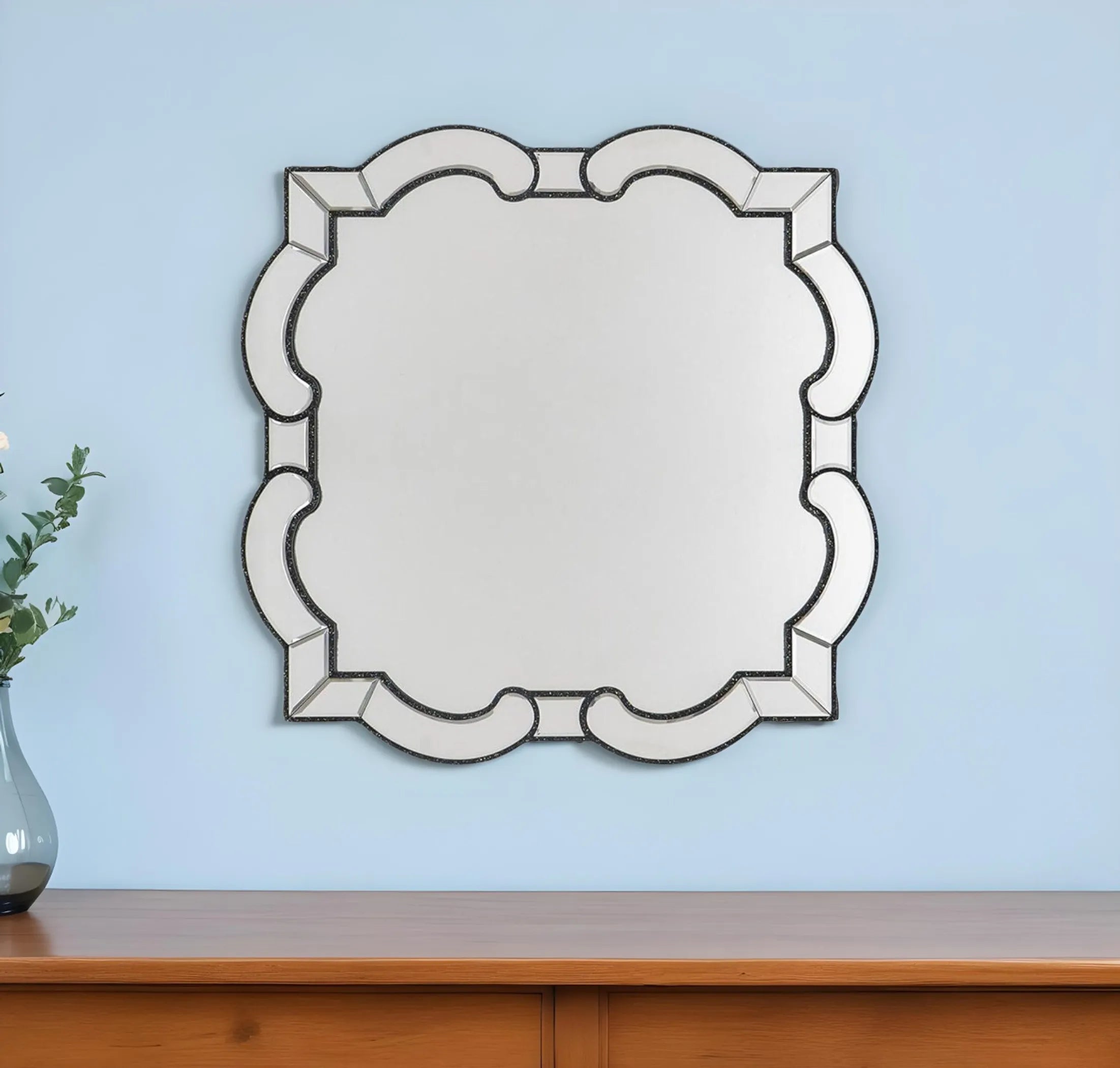 Decorative wall mirror with scalloped edge on a light blue wall above a wooden surface.