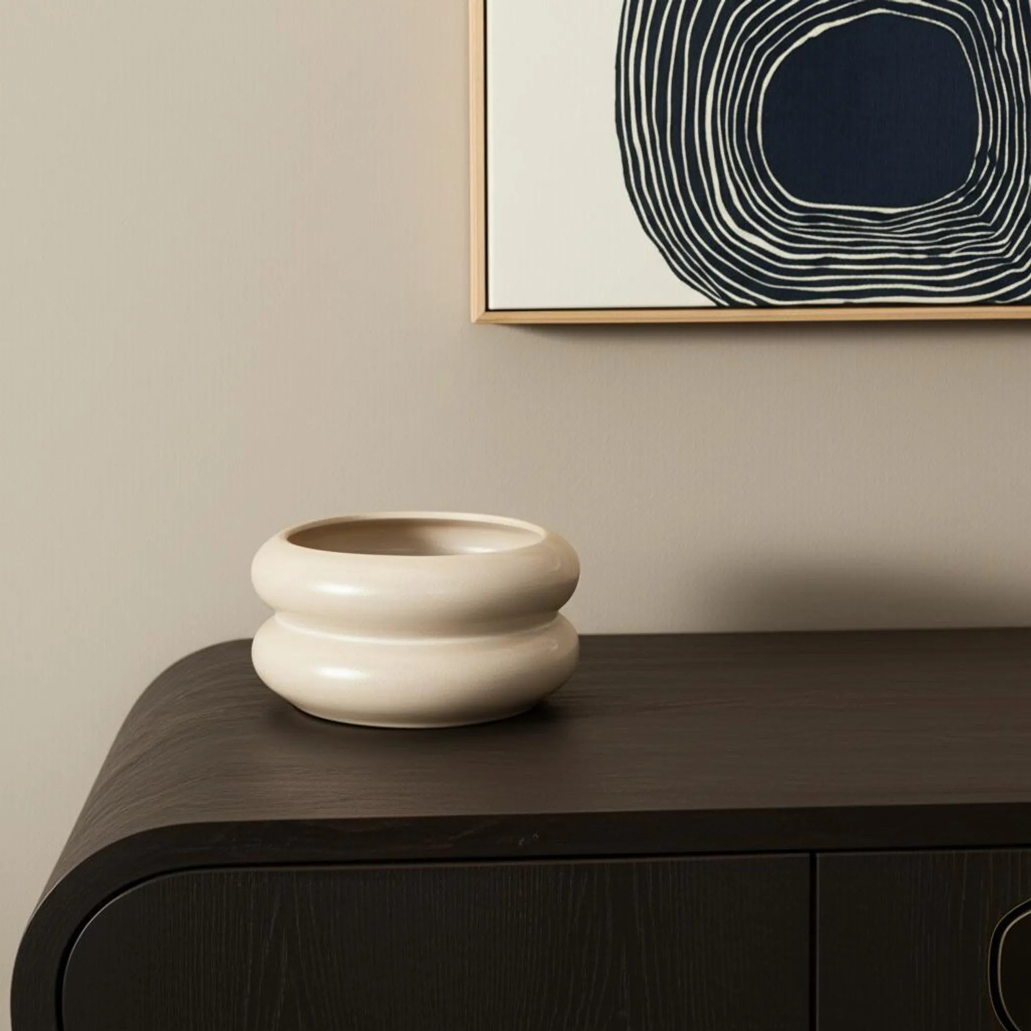 Ceramic vase on a dark wooden surface with abstract art in the background
