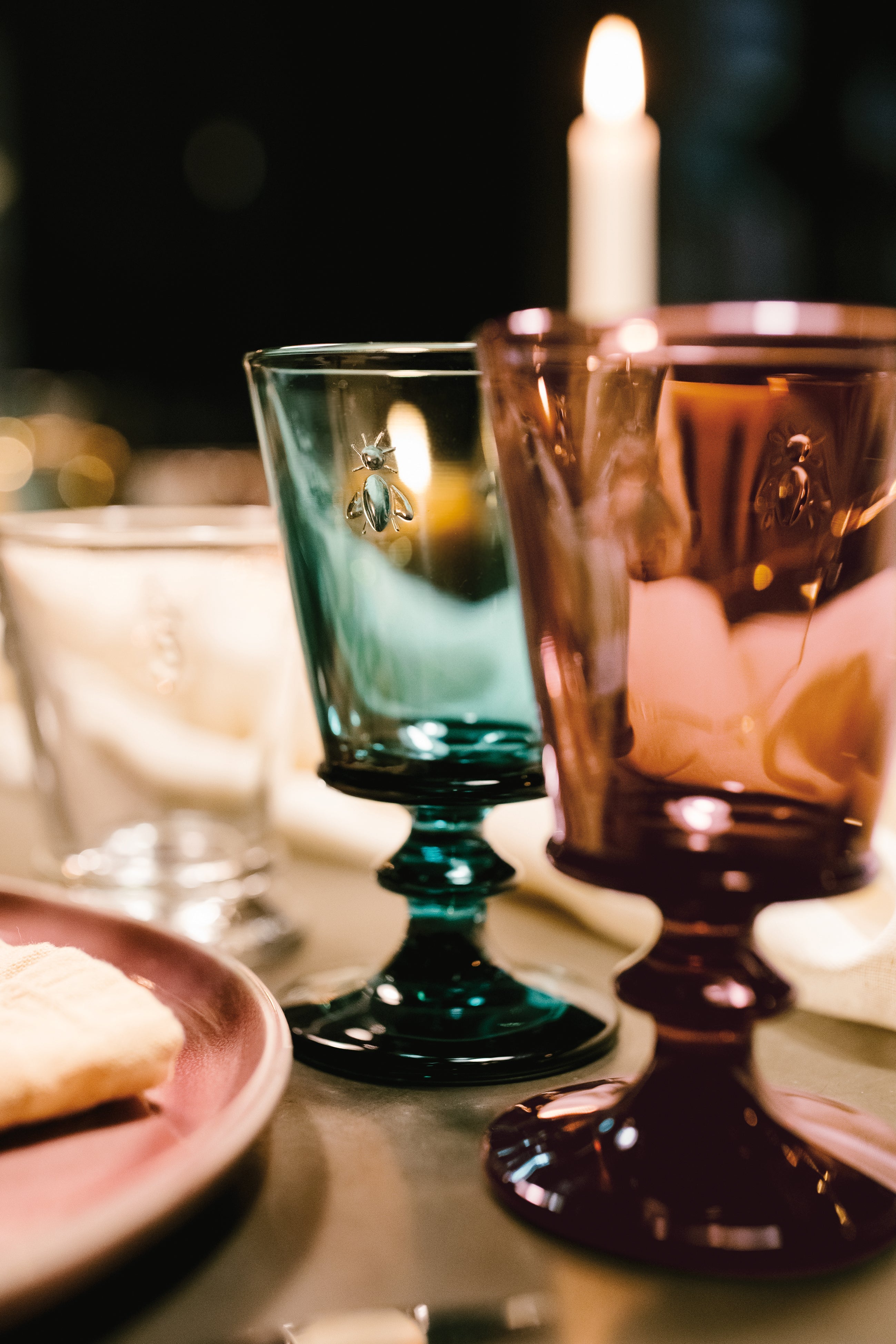 Two colorful glasses on a table with a blurred candle in the background