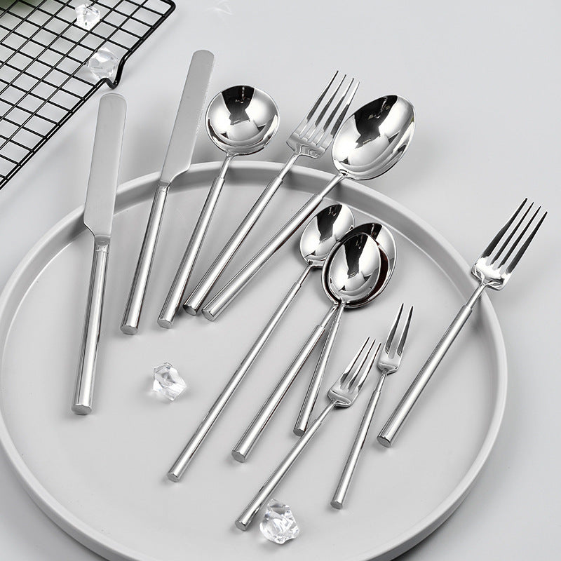 Set of silver cutlery including knives, spoons, and forks on a white plate with a cooling rack in the background.