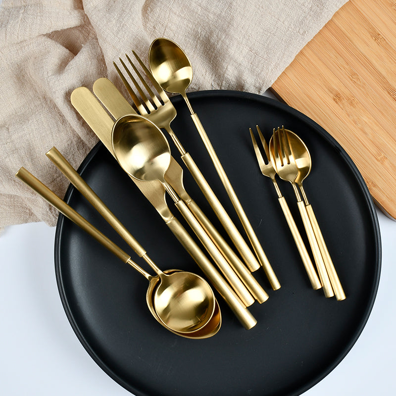 Gold cutlery set on a black plate with a wooden board and beige fabric in the background.