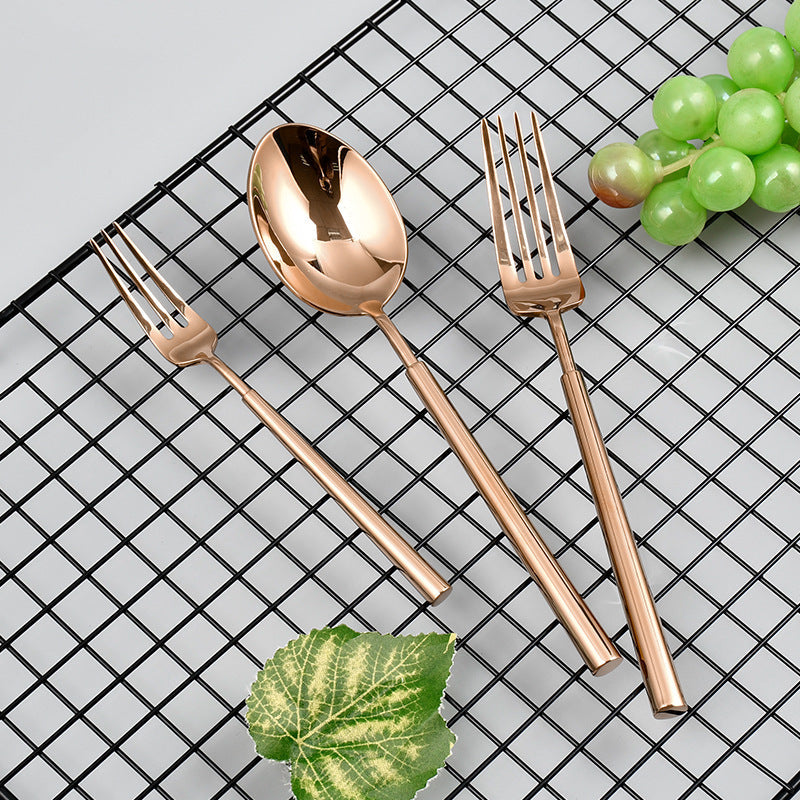 Rose gold cutlery set on a black grid background with grapes and leaves.