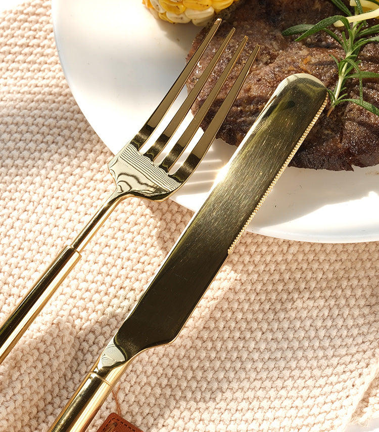Gold knife and fork set on a textured surface with a plate of food in the background
