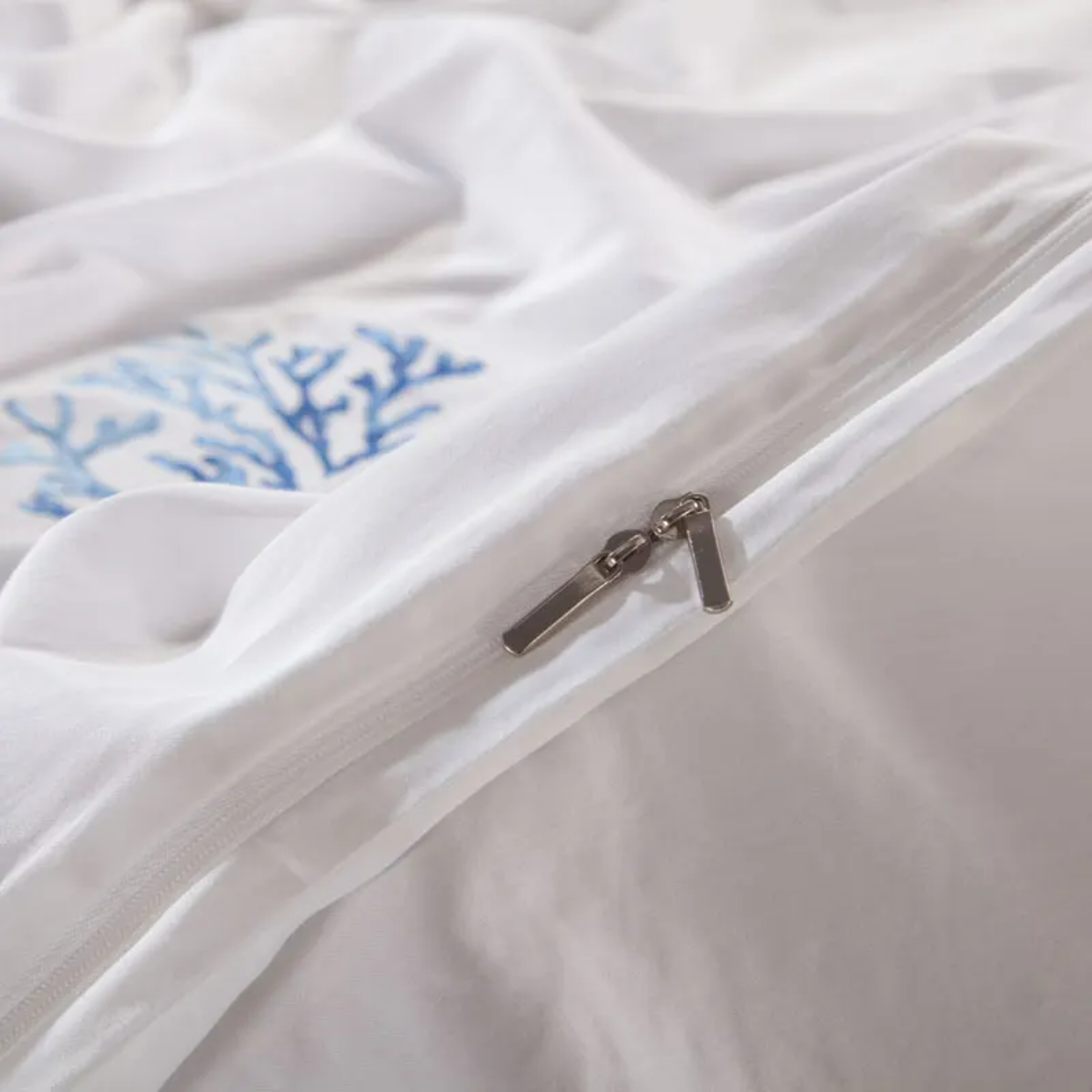 Close-up of a white comforter with blue floral embroidery and a zipper.