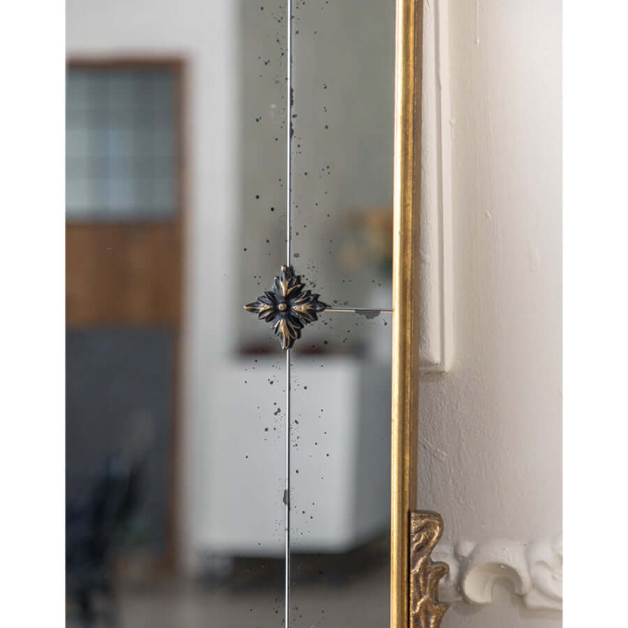 Decorative mirror with gold frame and intricate design on a white wall.