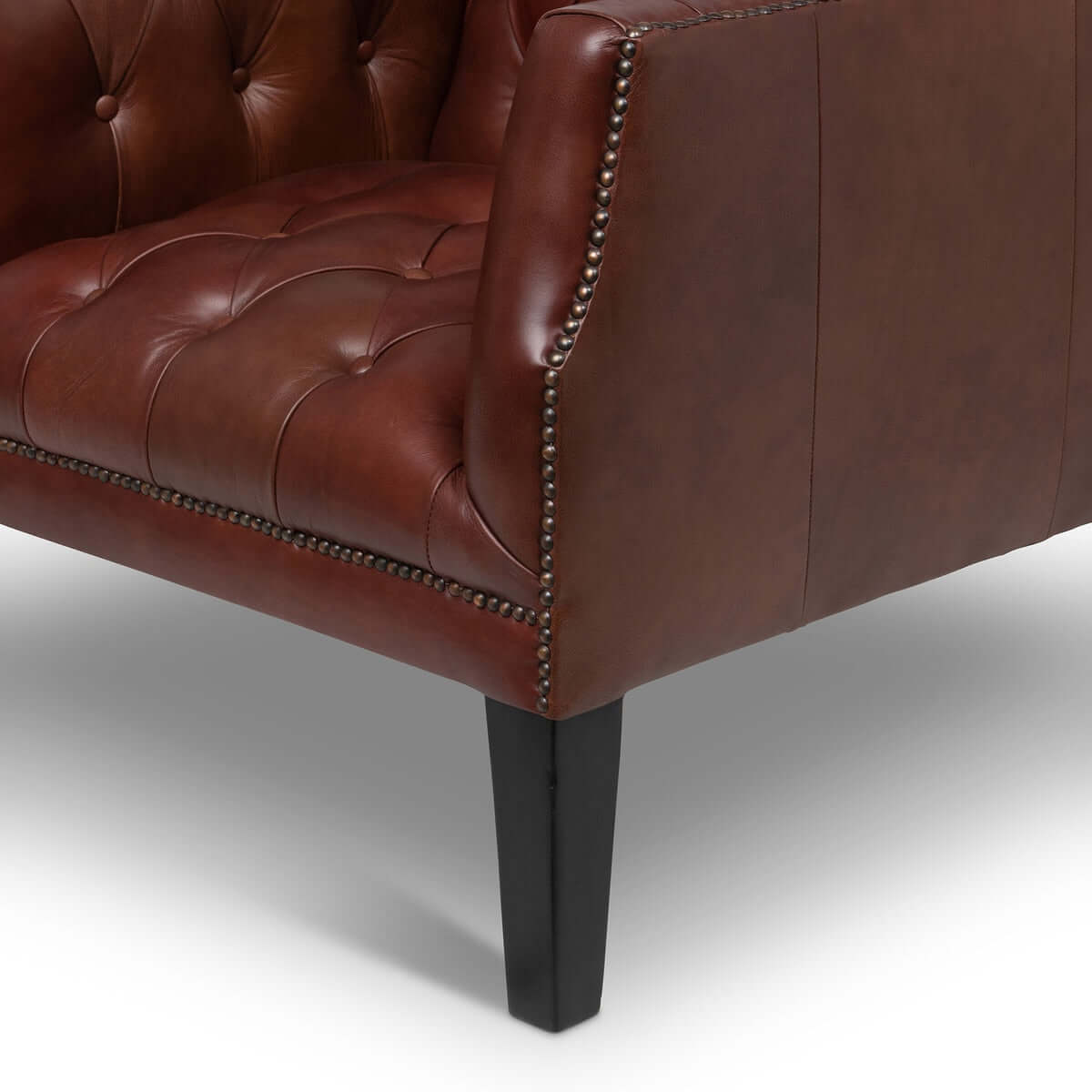 Close-up of a brown tufted leather armchair with black legs on a white background