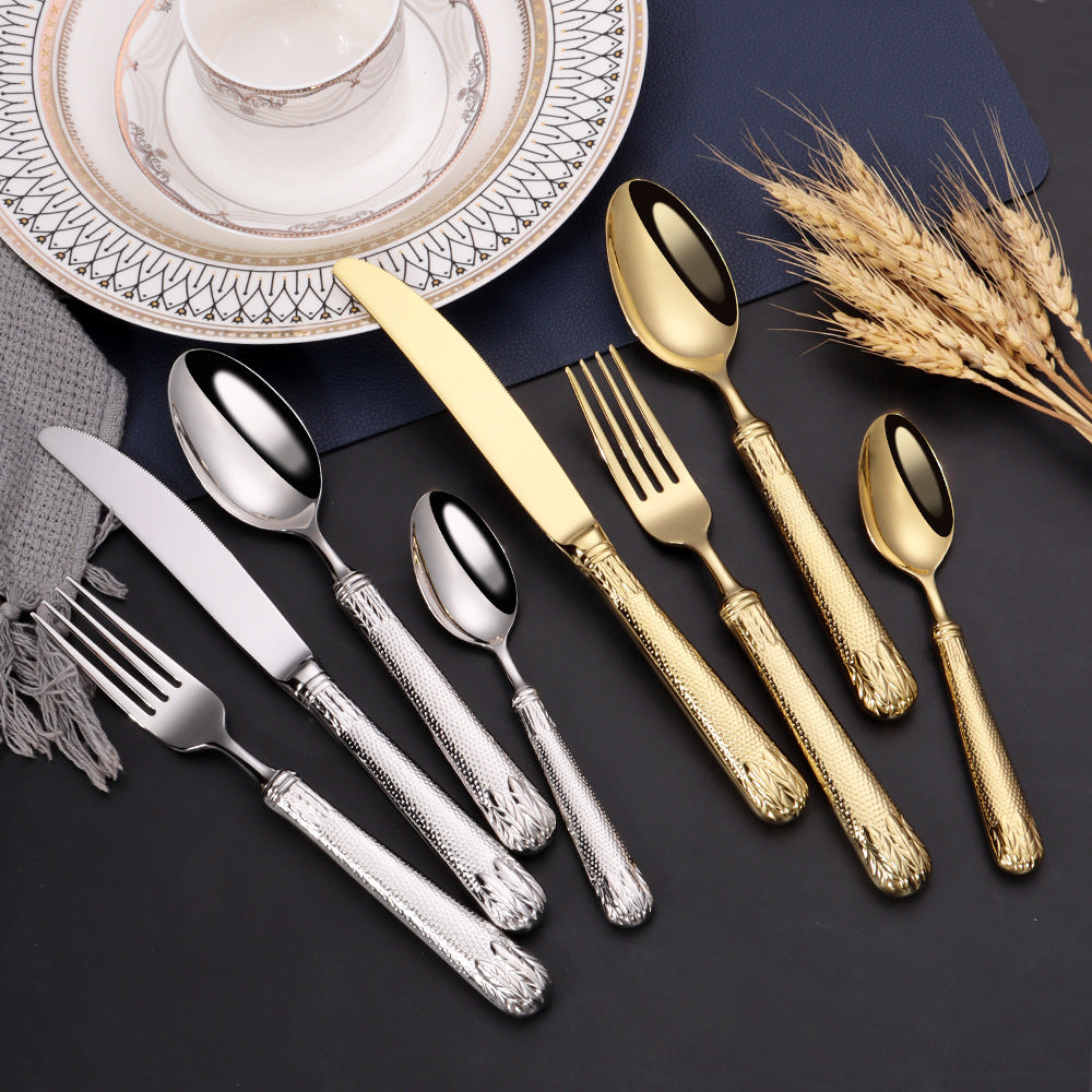 Set of silver and gold cutlery on a dark surface with decorative plates and wheat.