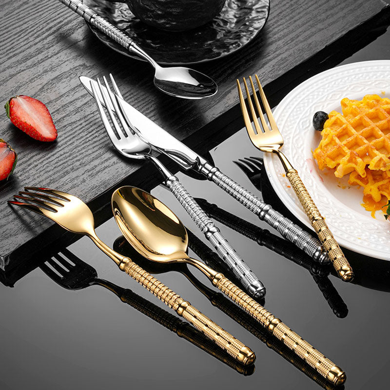 Set of gold and silver cutlery on a dark surface with a plate of food and strawberries.