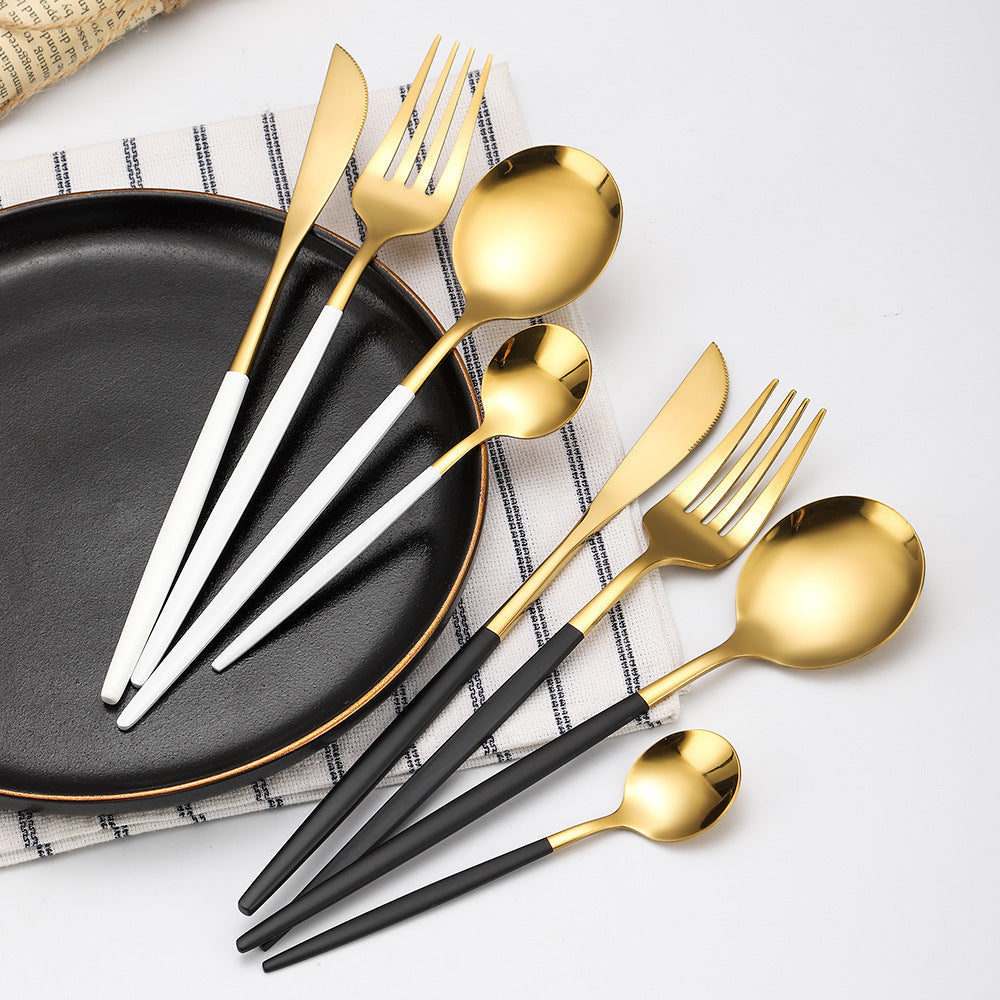 Gold and black cutlery set on a white surface with a black plate.