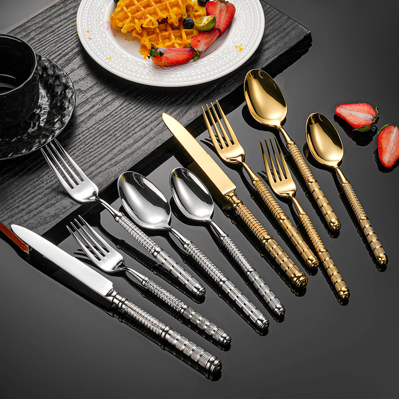 Set of gold and silver flatware on a dark surface with a plate of waffles and strawberries.
