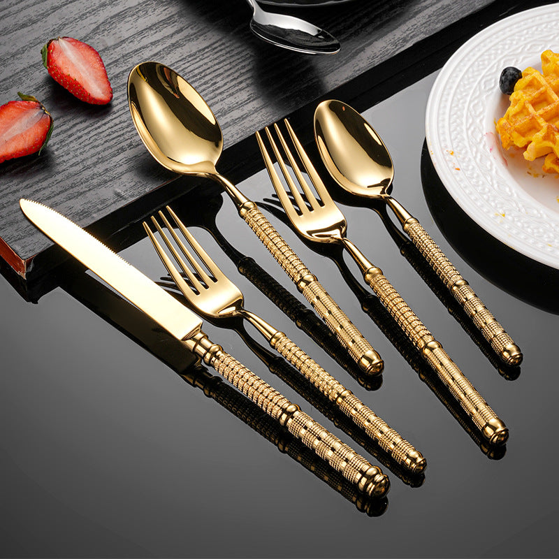 Set of gold cutlery on a dark surface with waffles and strawberries in the background