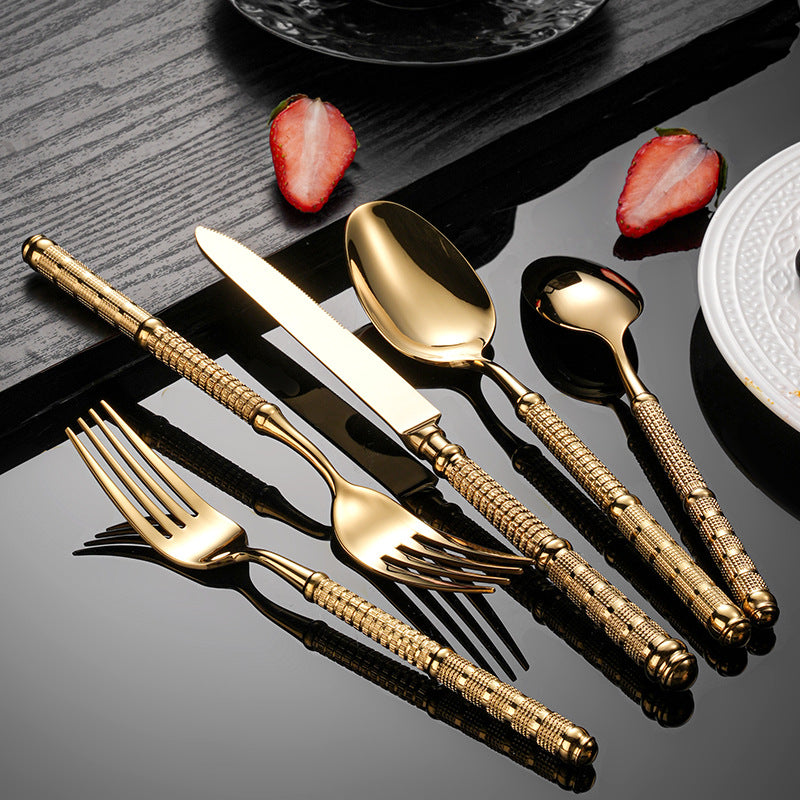 Gold cutlery set on a dark surface with strawberries and a plate.