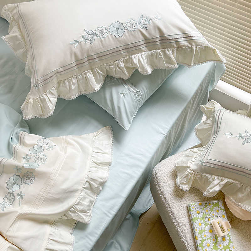 Light blue bedding set with white ruffled pillows and floral embroidery on a bed.