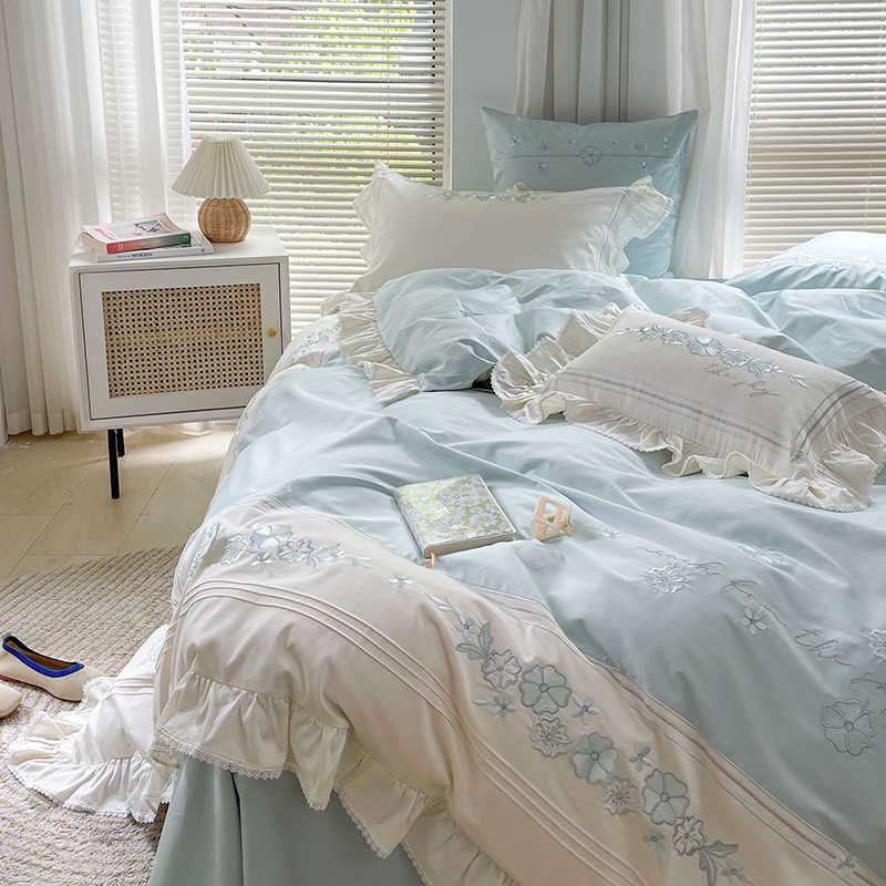Bedroom with light blue bedding and white pillows, featuring a side table with a lamp.