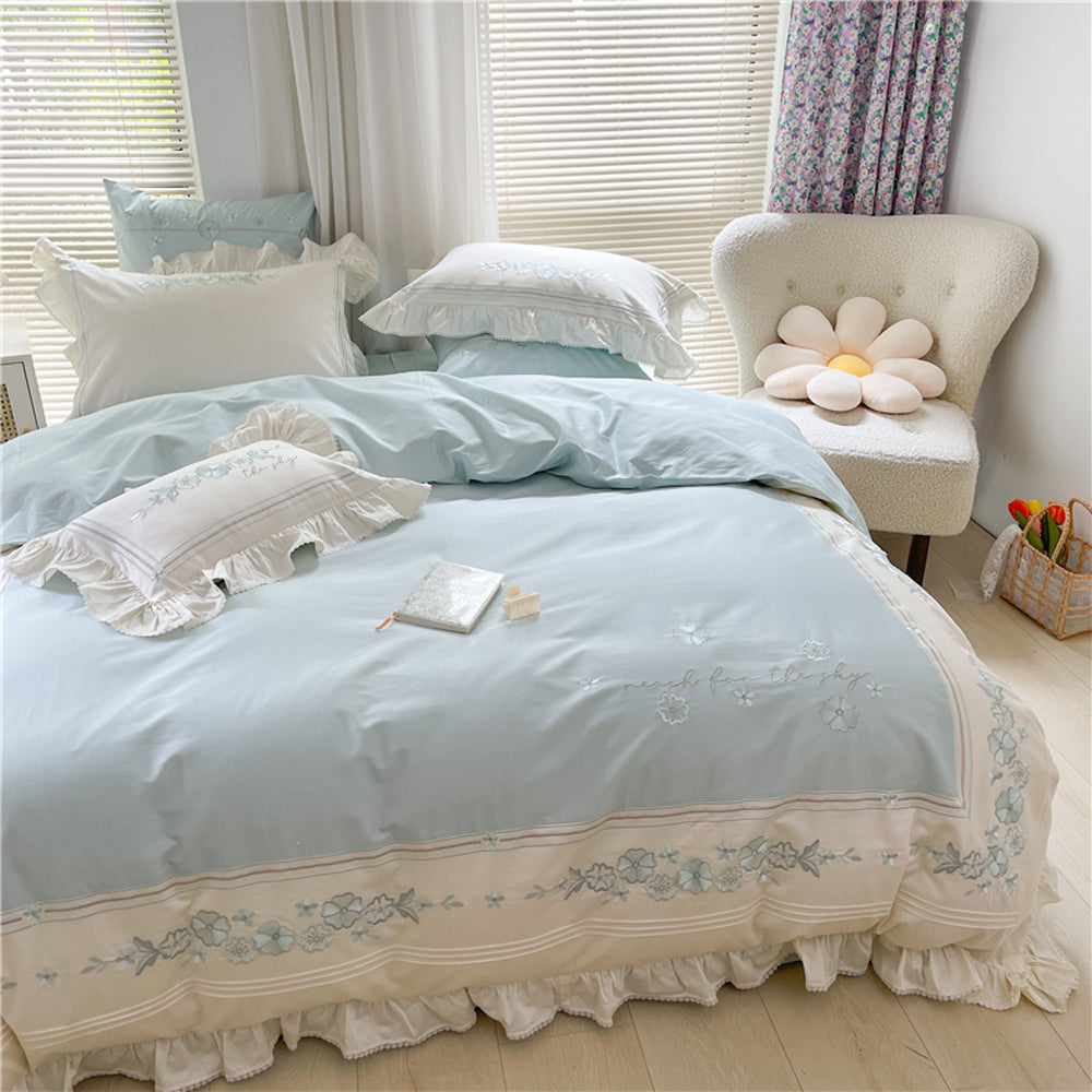 Light blue floral embroidered bedding set in a bedroom with a chair and decorative pillow.
