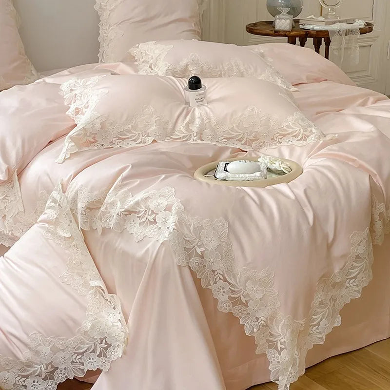 Pink lace bedspread on a bed with a small table and items on top.