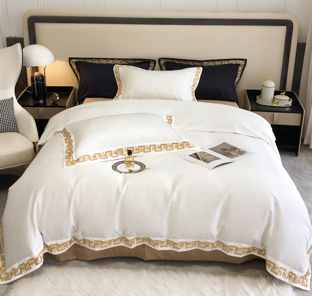 White bedspread with gold trim on a neatly made bed in a bedroom setting.