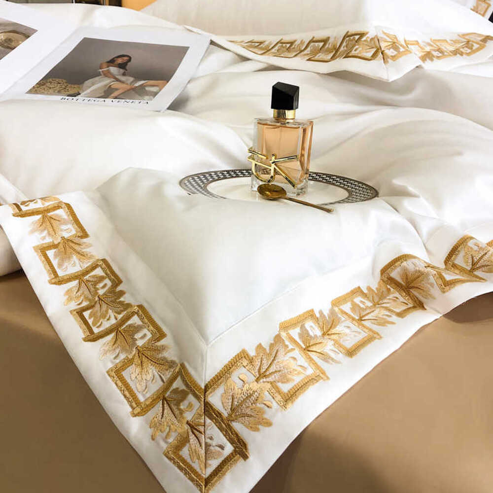 Decorative bedspread with gold embroidery on a bed, featuring a bottle of perfume.