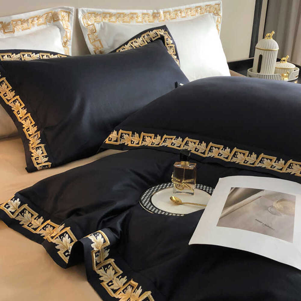 Black bedding set with gold embroidery on a bed, featuring a magazine and small decorative items.
