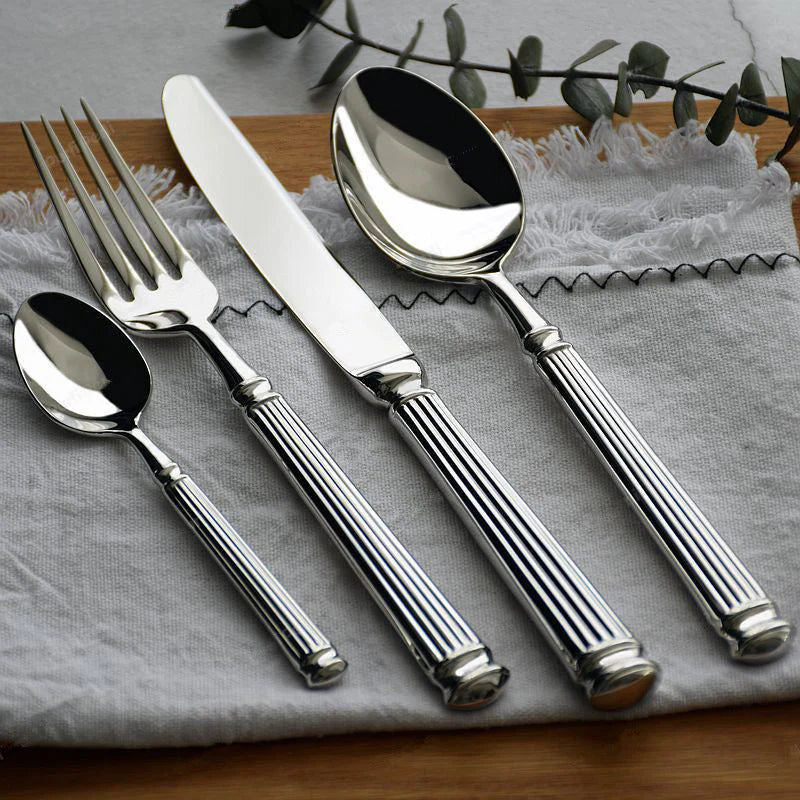 Silver cutlery set on a textured surface with a branch in the background