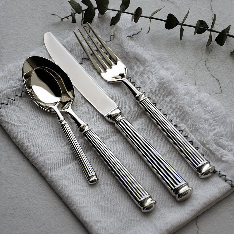 Silver cutlery set on a textured gray surface with green leaves.