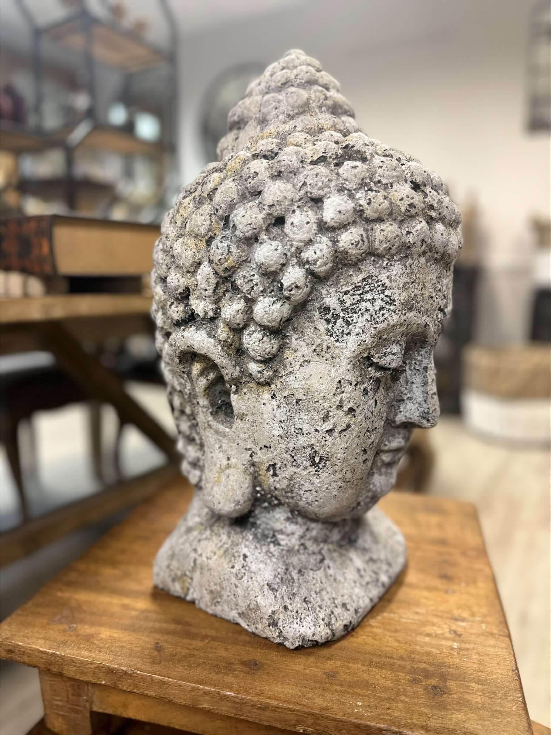 Stone Buddha head sculpture on a wooden table with a blurred indoor background