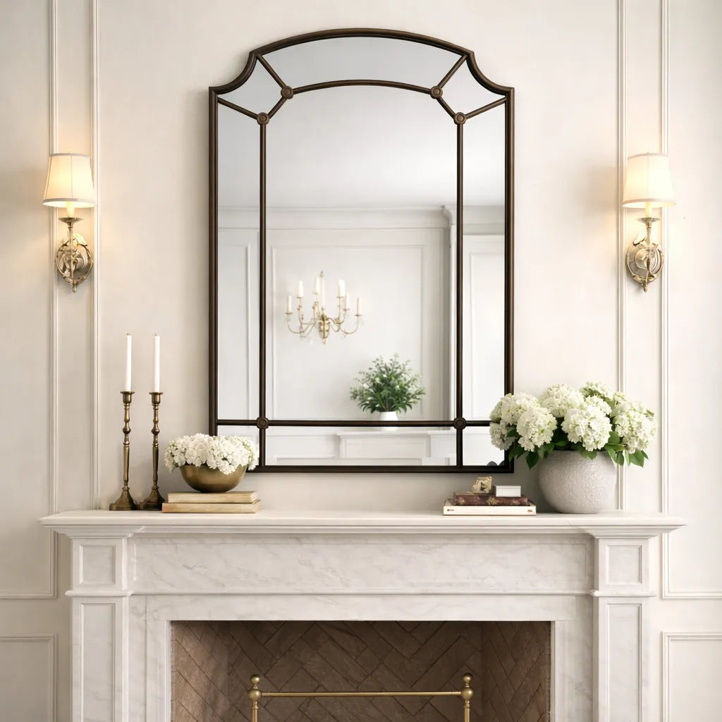Decorative mirror above a fireplace with candles and flowers on a mantel.