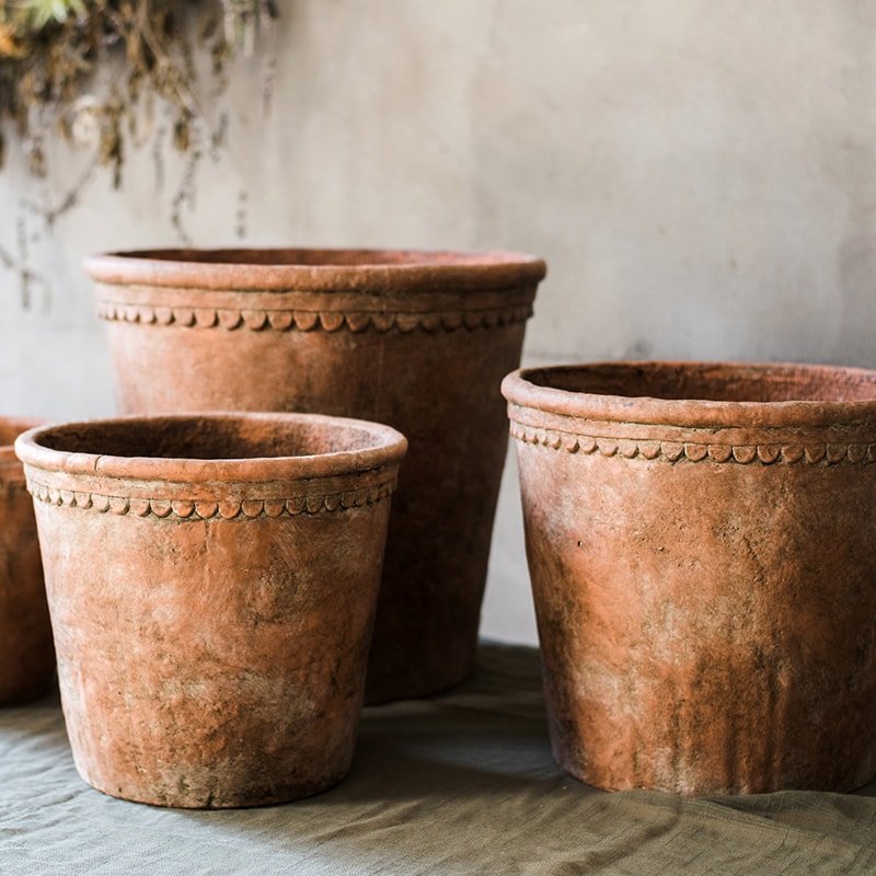 Four rustic terracotta planters in varying sizes arranged on a draped fabric surface against a neutral textured wall.