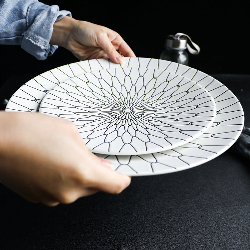 Two ceramic plates with black geometric patterns held by a person on a dark surface.