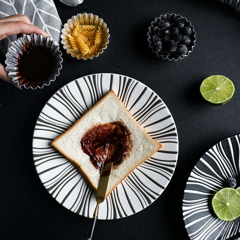Toast with chocolate spread on a black and white plate with a lime wedge and blackberries in the background.